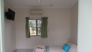 A bedroom with a bed, a window with curtains, an air conditioning unit, and a television on the wall. - Ingham Tourist Park (Ingham)