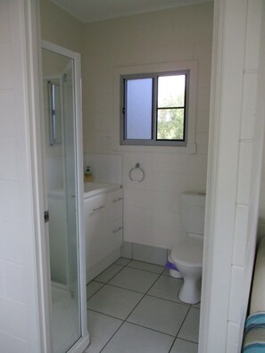 A small, clean bathroom with a toilet, a sink, and a window. - Ingham Tourist Park (Ingham)