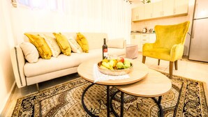 A living room with a sofa, a yellow armchair, a coffee table with fruit, and a kitchen in the background. - Premium suites on Beach Ben Yehuda 43 (Tel Aviv)