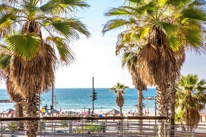 A beach scene with palm trees, a beach umbrella, and a view of the ocean. - Premium suites on Beach Ben Yehuda 43 (Tel Aviv)
