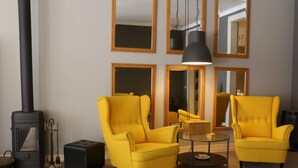 Una sala de estar moderna con dos sillones amarillos, una mesa de centro de vidrio y una lámpara colgante negra. Se observa una chimenea negra a la izquierda.
