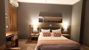 Habitación de hotel con una cama grande, cabecero de madera, mesitas de noche con lámparas, un espejo sobre la cama y un armario de madera.