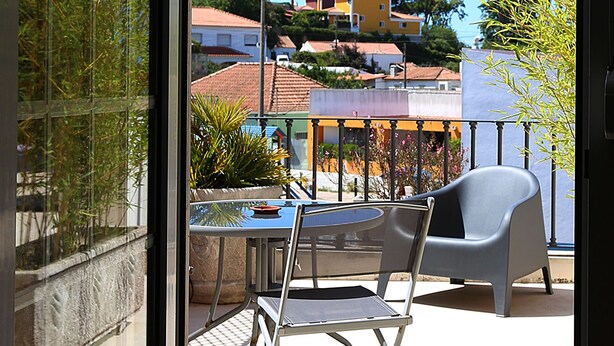 Un balcón con mesa y sillas, con vistas a una zona residencial con casas y árboles.