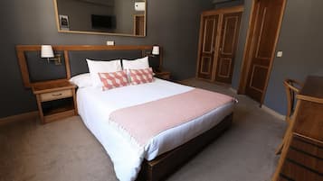 A neatly arranged bedroom with a large bed, wooden headboard, bedside tables, a mirror, and a wardrobe.