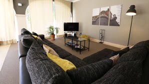 Una sala de estar con un sofá, un televisor, una mesa de centro de vidrio y una lámpara de pie.