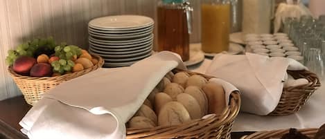 Une table de buffet avec des paniers de pain, des assiettes et une variété de fruits.
