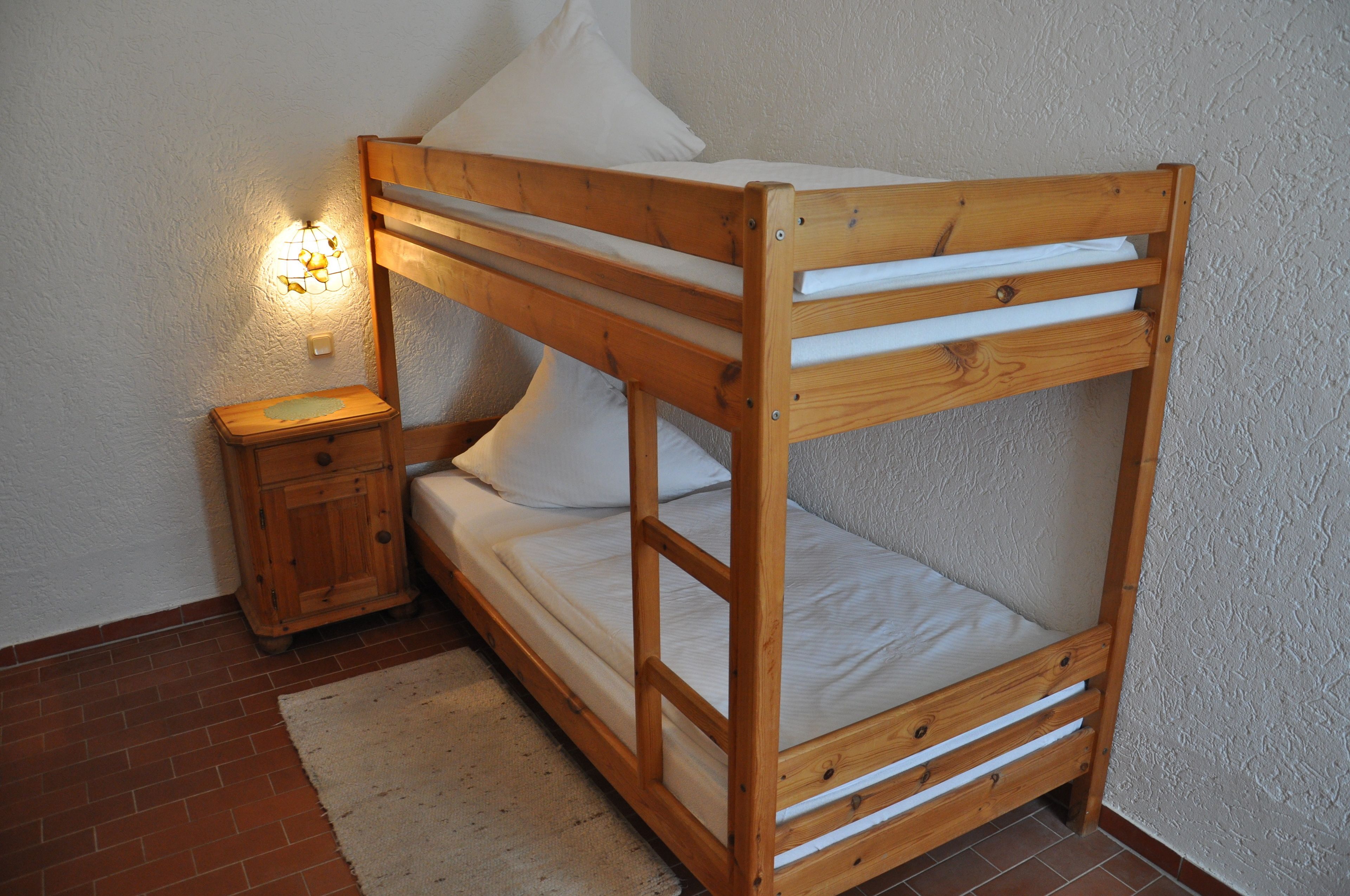 Una cama litera de madera con una mesita de noche y una lámpara.