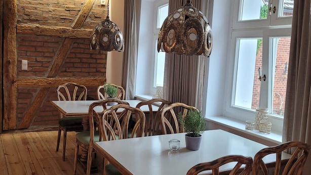 Een eetgedeelte met houten tafels en stoelen, een bakstenen muur en grote ramen met gordijnen.