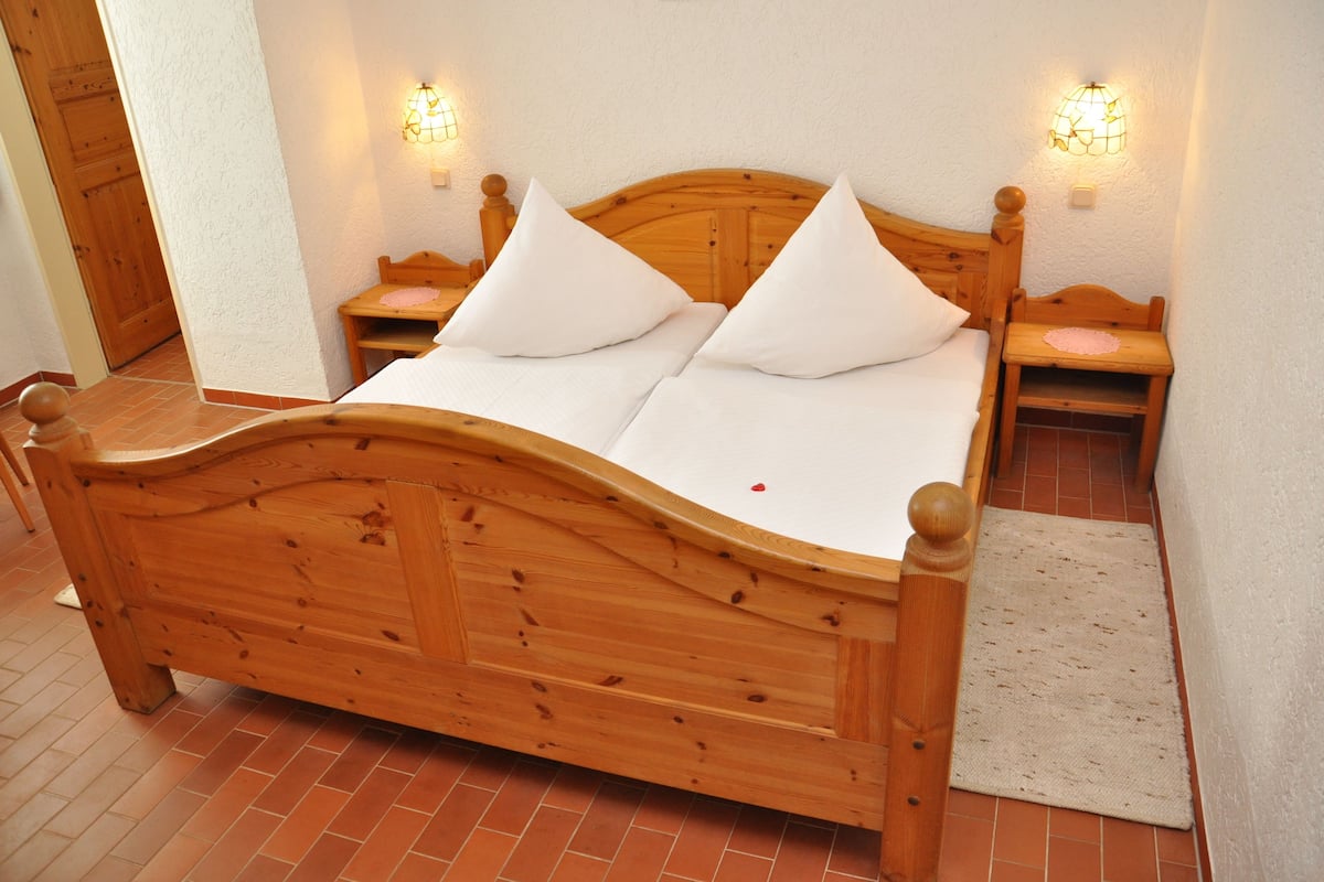 Un lit en bois avec deux oreillers, une table de chevet et une lampe fixée au mur.