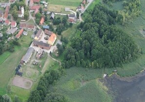 Vista aérea de una zona rural con un conjunto de edificios, incluyendo una casa grande con techo rojo, rodeada de campos y un bosque denso.