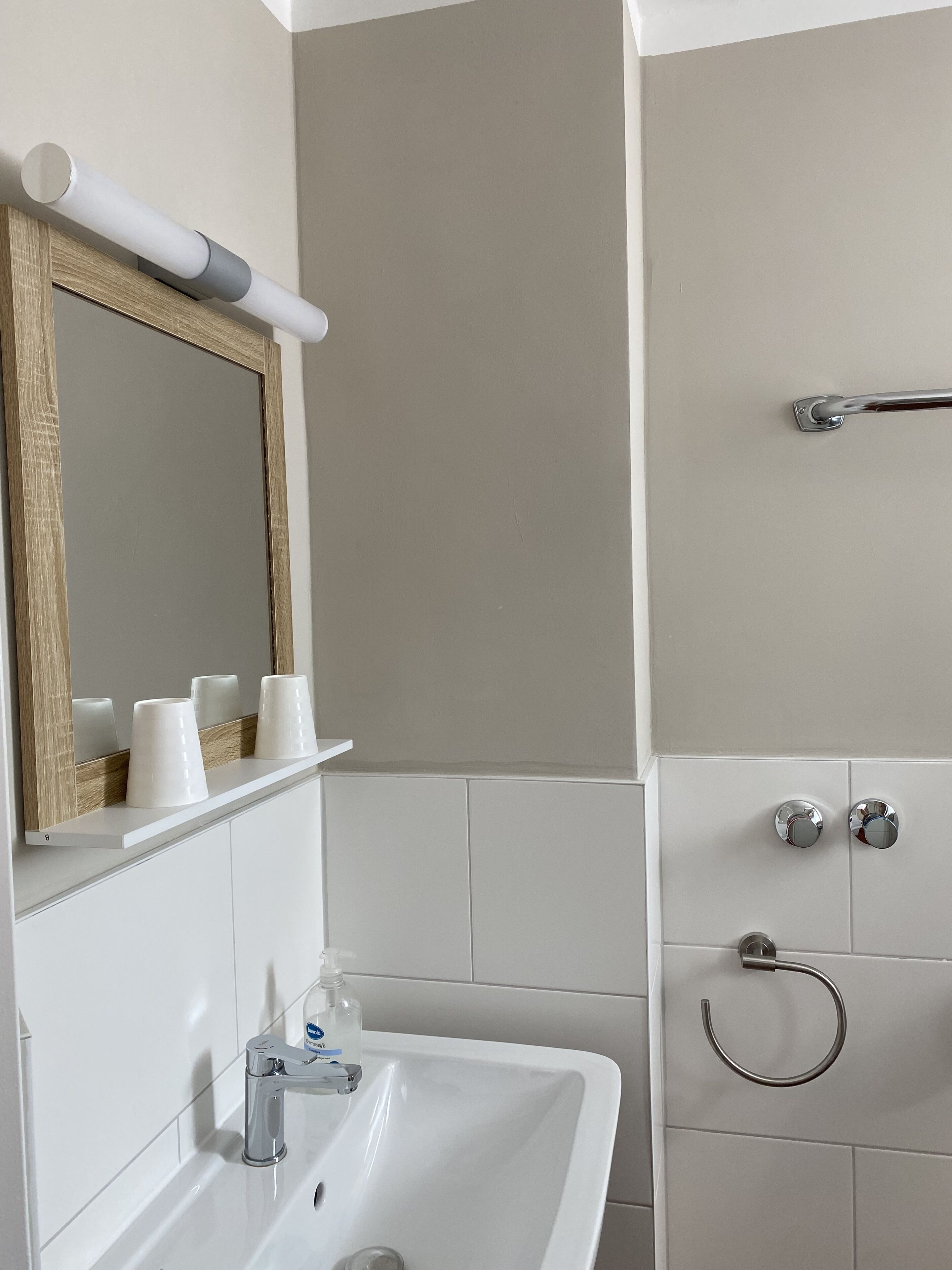A bathroom with a white sink, a mirror with a wooden frame, and a shower area with a grab bar.