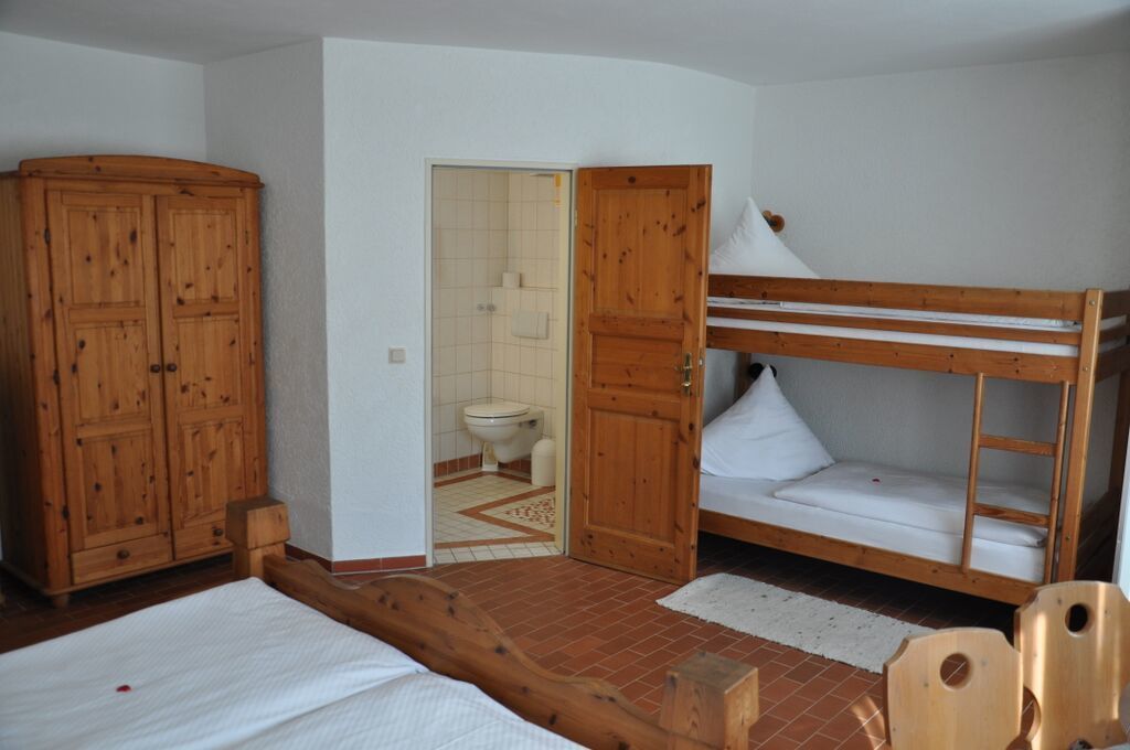 A small, compact room with a bunk bed, wooden wardrobe, and a bathroom visible through an open door.