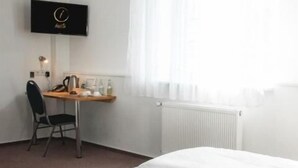 A hotel room with a bed, a desk, a chair, a TV, and a window with curtains. - Hotel Imota (Neuwied)
