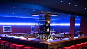 A bar area with a long counter, red bar stools, and a tiled floor. - Hotel Imota (Neuwied)