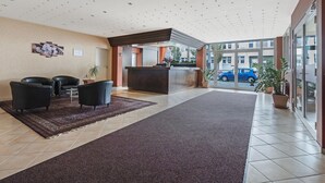 A hotel lobby with a reception desk, seating area, and large windows. - Hotel Imota (Neuwied)
