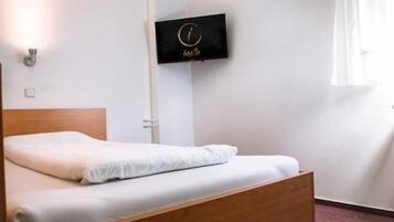A single bed with a wooden headboard in a room with white walls. A flat-screen TV is mounted on the wall above the bed.