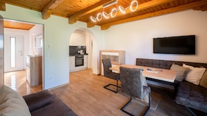 A modern living room with a wooden ceiling, a dining area with a table and chairs, a sofa, and a TV mounted on the wall. - Erlebnisbauernhof Tschom (Sankt Kanzian am Klopeiner See)