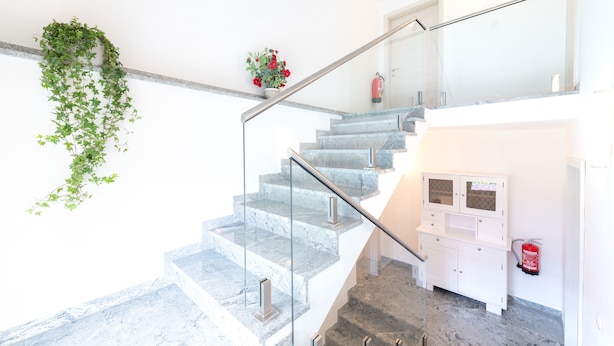 A modern staircase with glass railings, a fire extinguisher mounted on the wall, and a small potted plant on the landing. - Erlebnisbauernhof Tschom (Sankt Kanzian am Klopeiner See)
