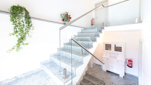 A modern staircase with glass railings, a fire extinguisher mounted on the wall, and a small potted plant on the landing. - Erlebnisbauernhof Tschom (Sankt Kanzian am Klopeiner See)