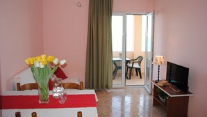 Une chambre d’hôtel avec un lit, une table ornée d’un vase de fleurs, une télévision et une porte-fenêtre coulissante donnant sur un balcon.