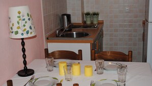 A dining area with a table set for four, a kitchen area with a sink and potted plants, and a lamp on the left. - Mime 2 (Omis)