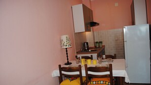 A small kitchen with a dining table, chairs, a refrigerator, and a cabinet. - Mime 2 (Omis)