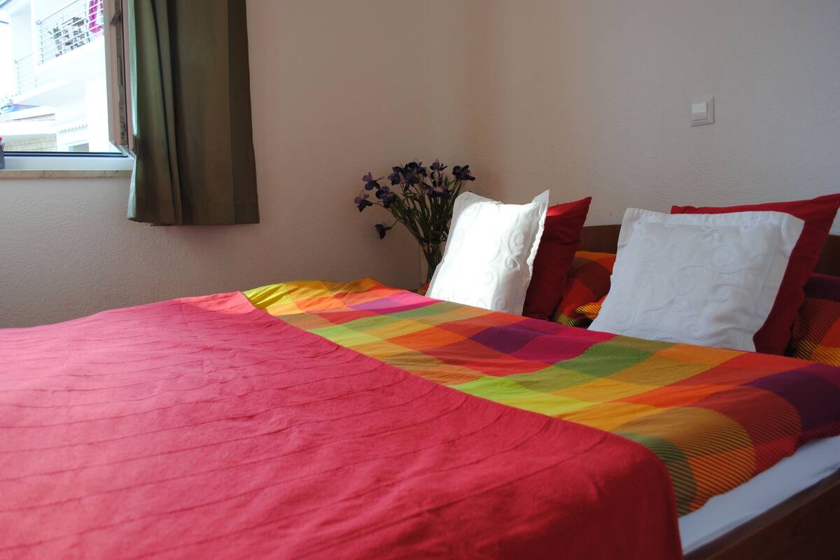 A bed with a colorful quilt, a vase with flowers, and a window with curtains.