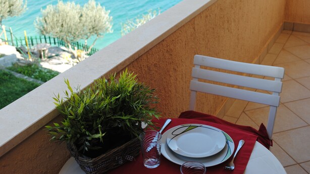A balcony with a table set for two, overlooking a body of water. - Mime 2 (Omis)