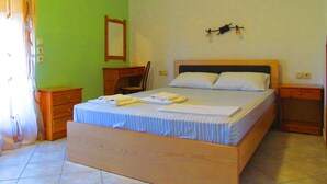 A bedroom with a wooden bed, a nightstand, a chair, a desk, and a mirror on the wall. - Pandora Studios (South Pelion)