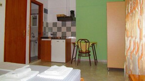 A compact hotel room with a kitchenette, a bed with neatly folded towels, and a chair. - Pandora Studios (South Pelion)