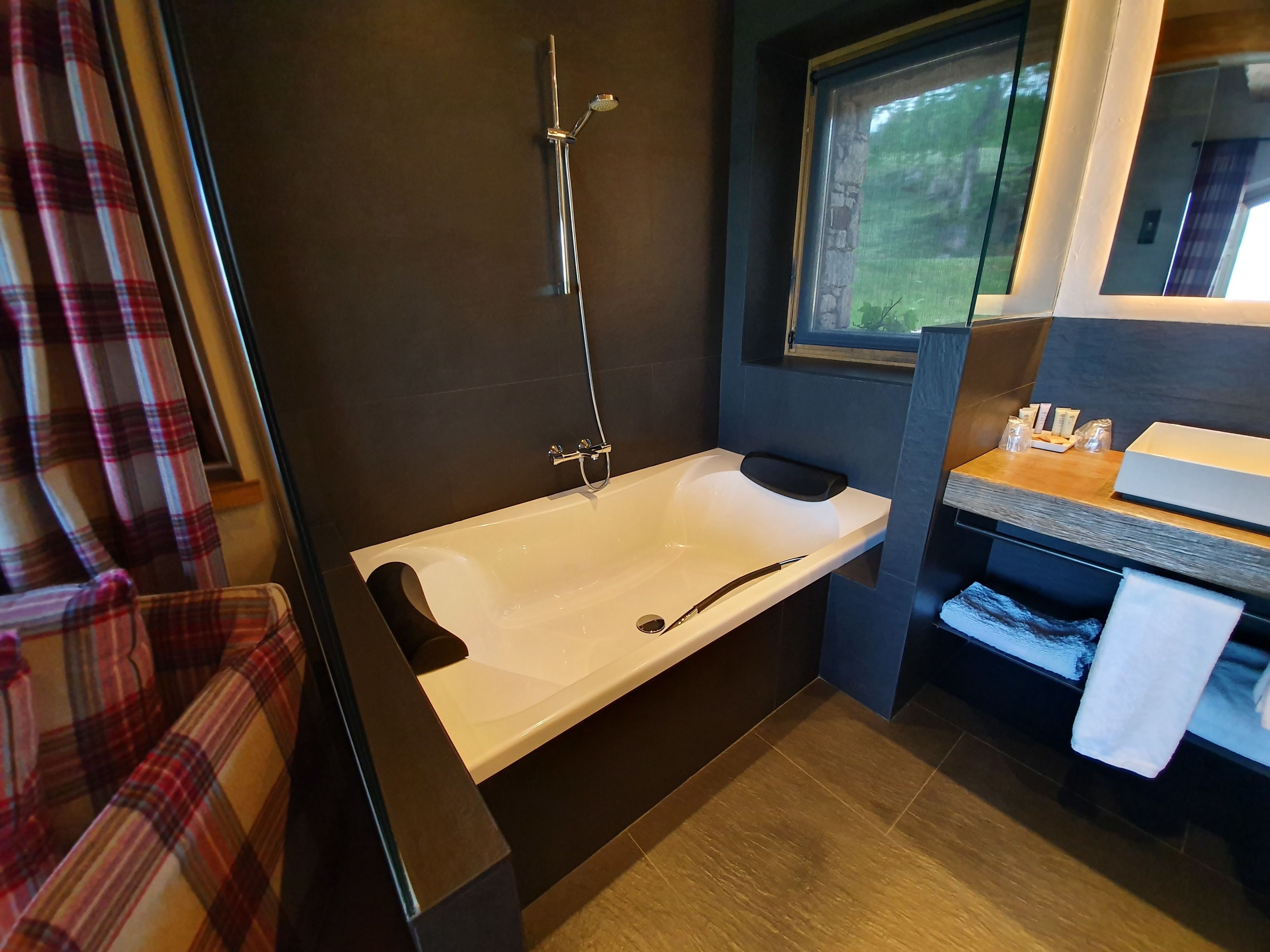 A modern bathroom with a bathtub, a shower, a vanity with a mirror, and a window providing a view of the outdoors.