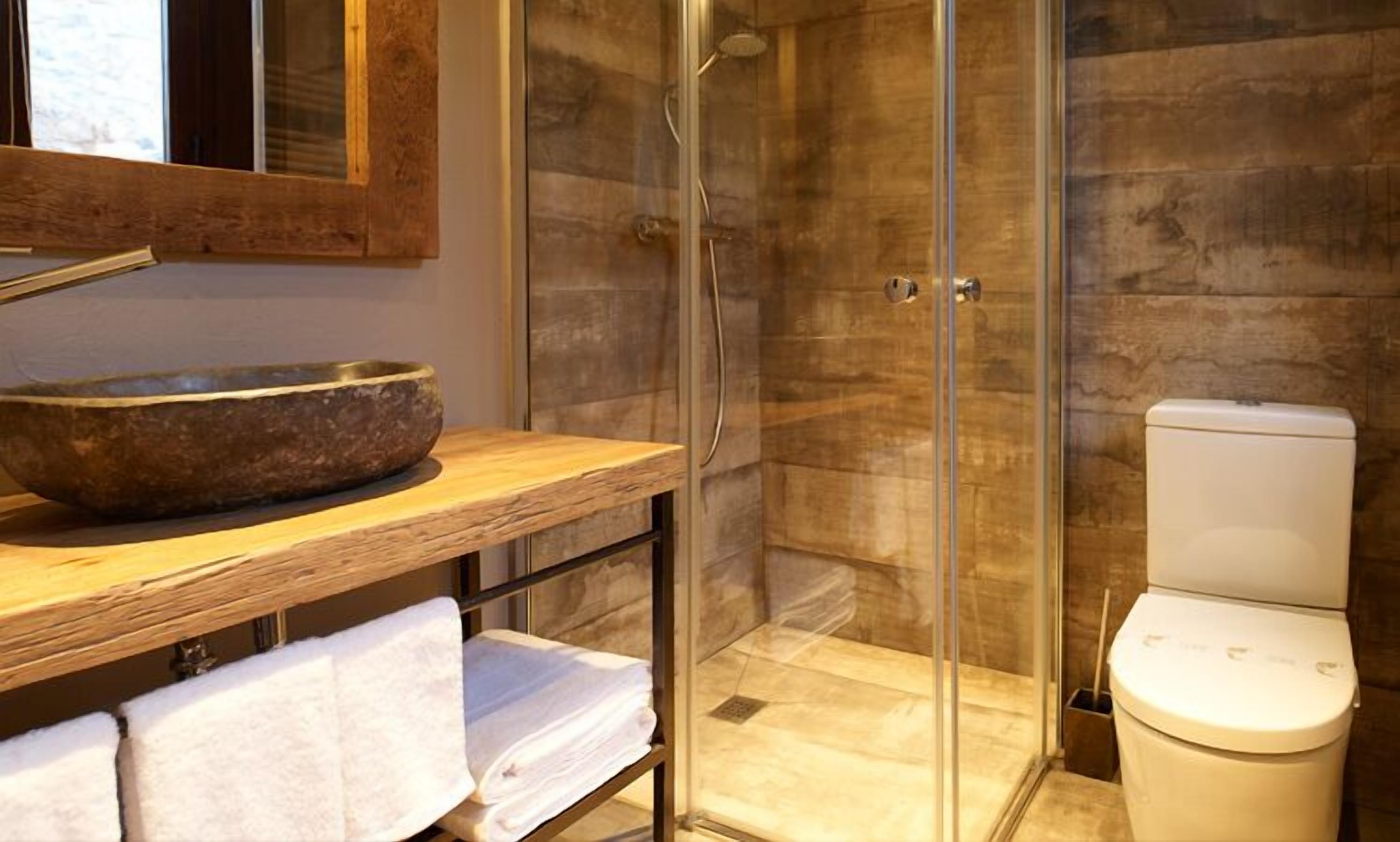 A bathroom with a wooden vanity, a stone basin, a glass shower enclosure, and a toilet.