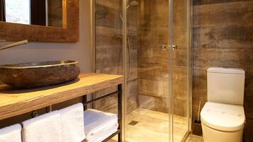 A bathroom with a wooden vanity, a stone basin, a glass shower enclosure, and a toilet.