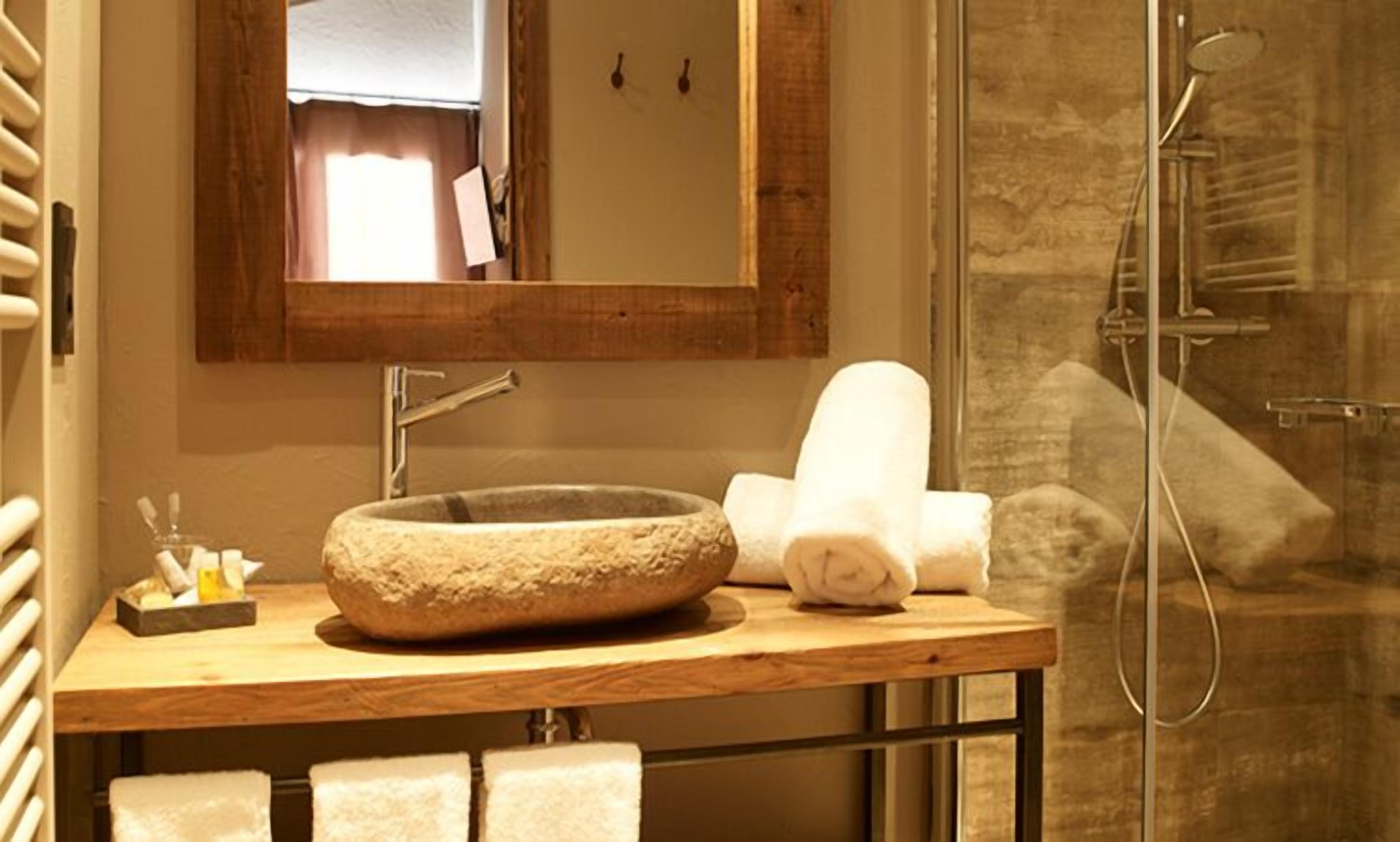 Een badkamer met een wasbak van steen, een spiegel en een douche.