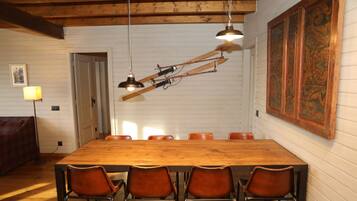 A dining area with a wooden table and six chairs, a large painting on the wall, and a lamp in the corner.