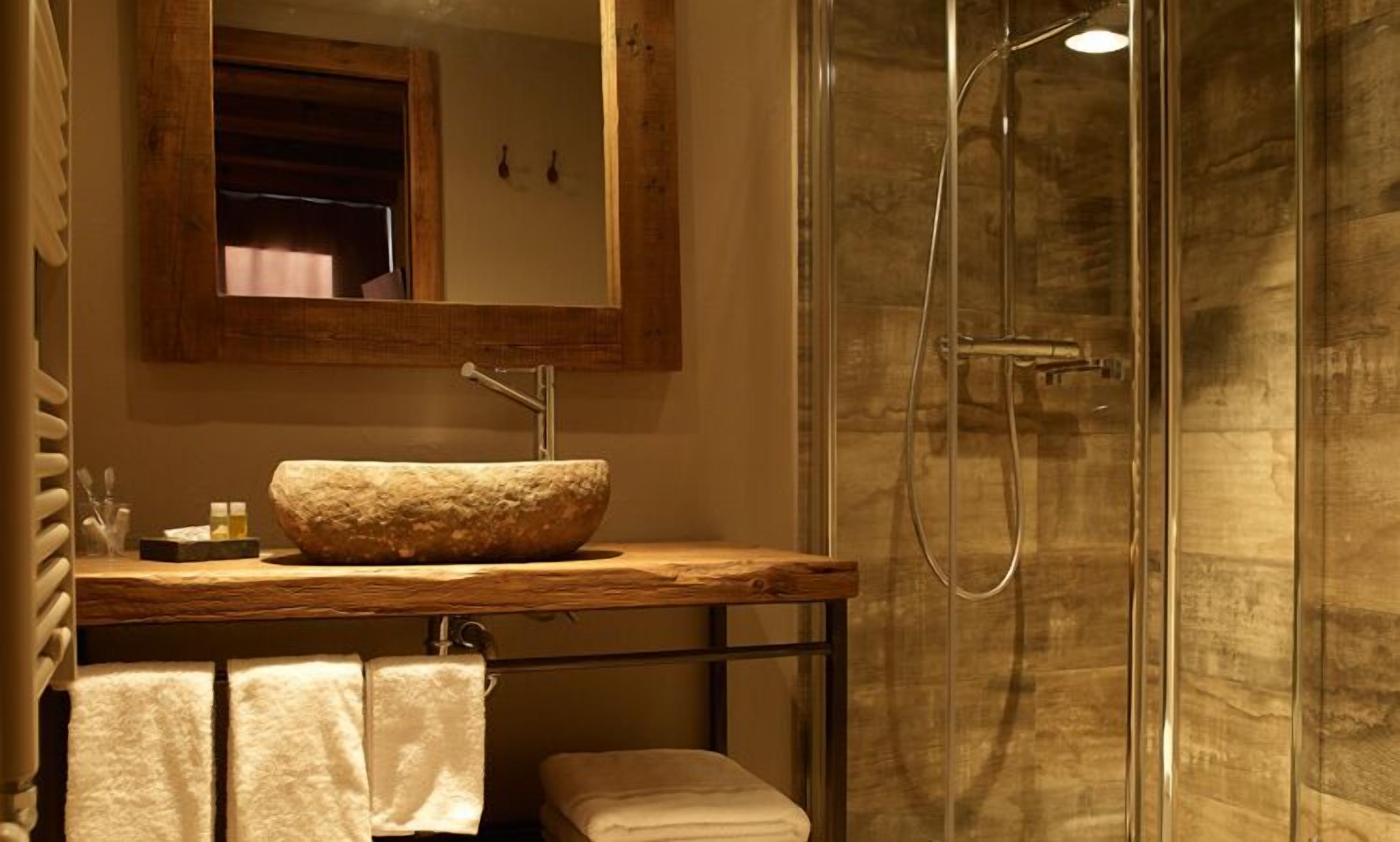 Une salle de bain avec un lavabo en pierre, un meuble-lavabo en bois, une cabine de douche en verre et un miroir au-dessus du lavabo.