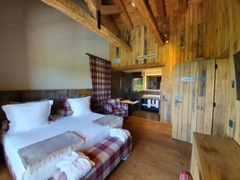 Un dormitorio de cabaña de madera con una cama grande, un banco y una mesita.