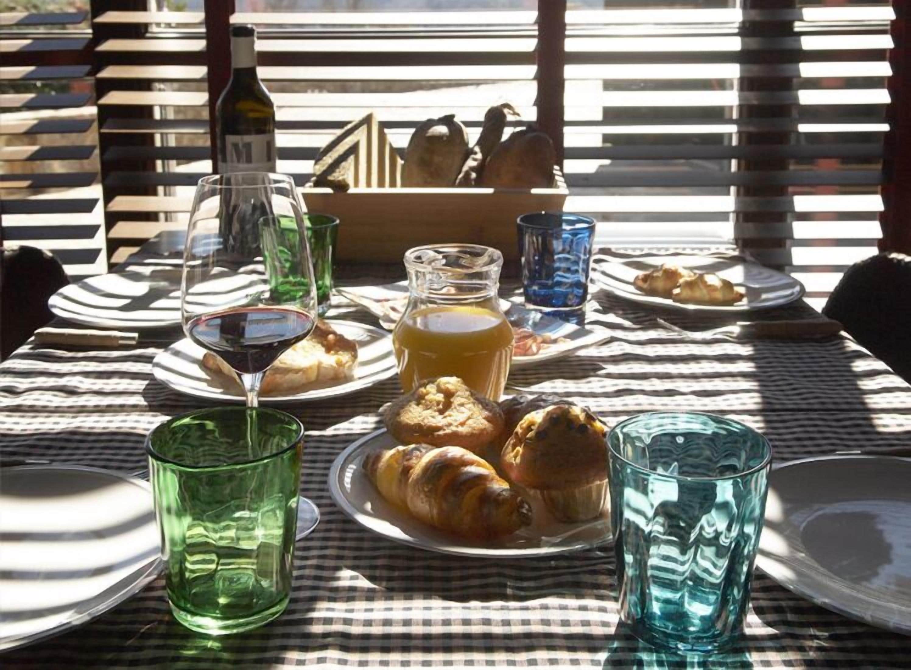 A table set for breakfast with croissants, a bottle of wine, and glasses of juice.