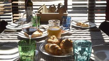 A table set for breakfast with croissants, a bottle of wine, and glasses of juice.