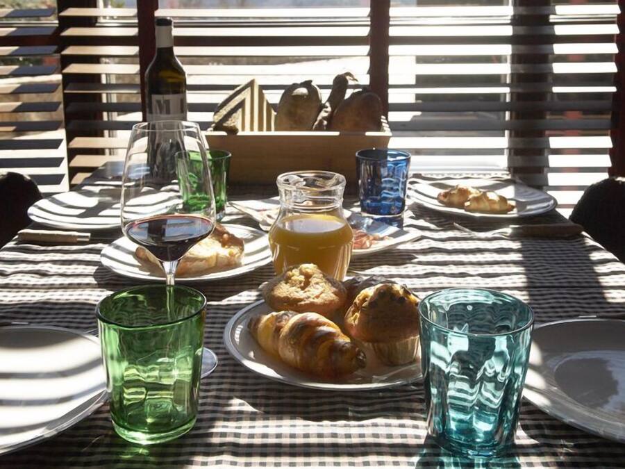 A table set for breakfast with croissants, a bottle of wine, and glasses of juice.