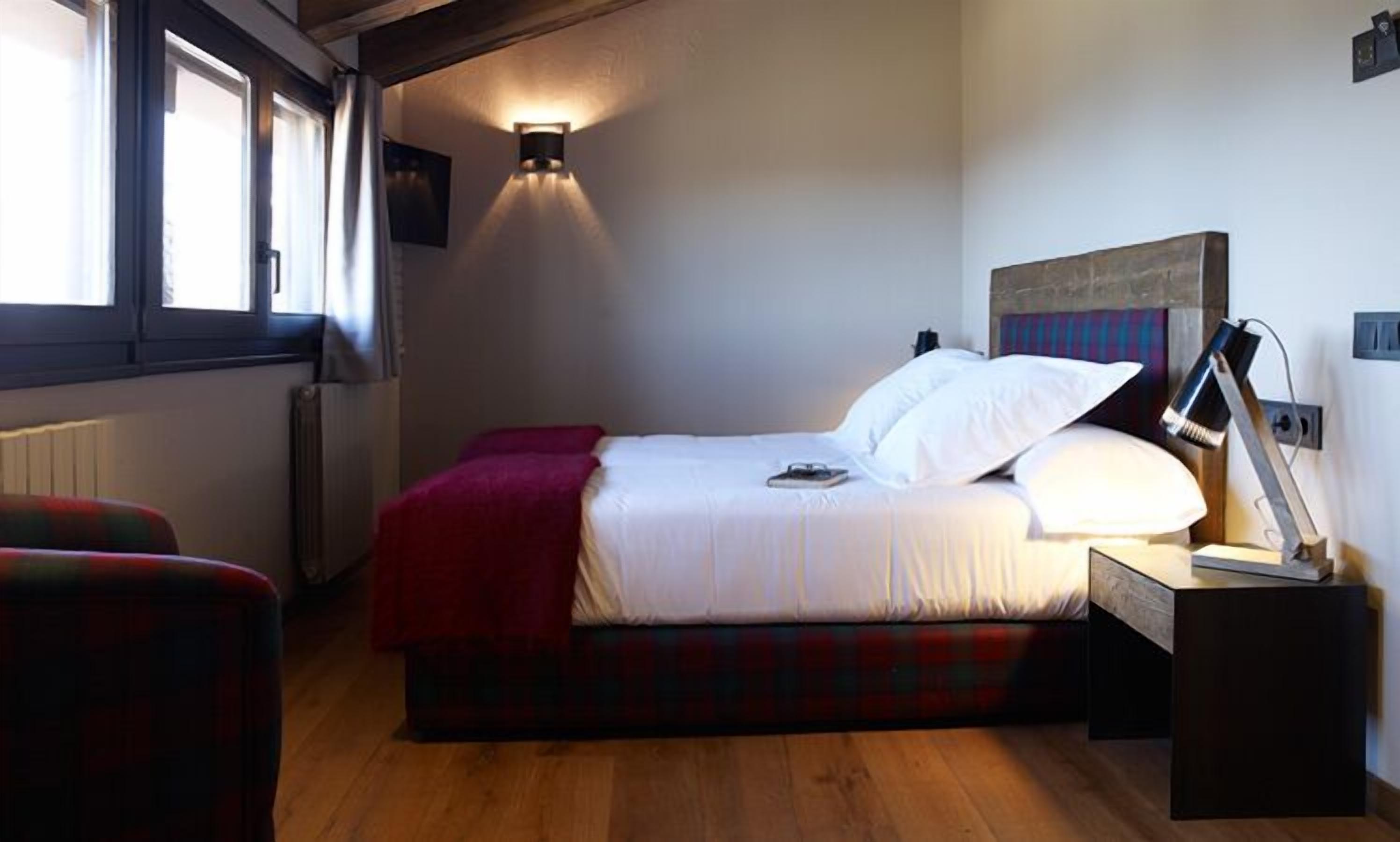 A bedroom with a bed, a red blanket, a bedside lamp, and a window with curtains.