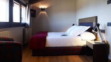 A bedroom with a bed, a red blanket, a bedside lamp, and a window with curtains.