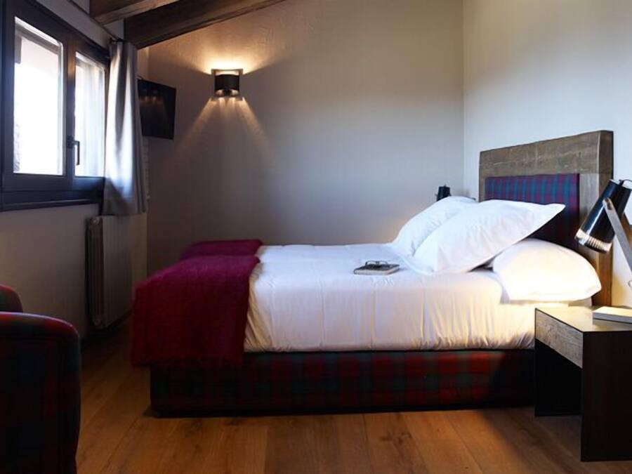 A bedroom with a bed, a red blanket, a bedside lamp, and a window with curtains.