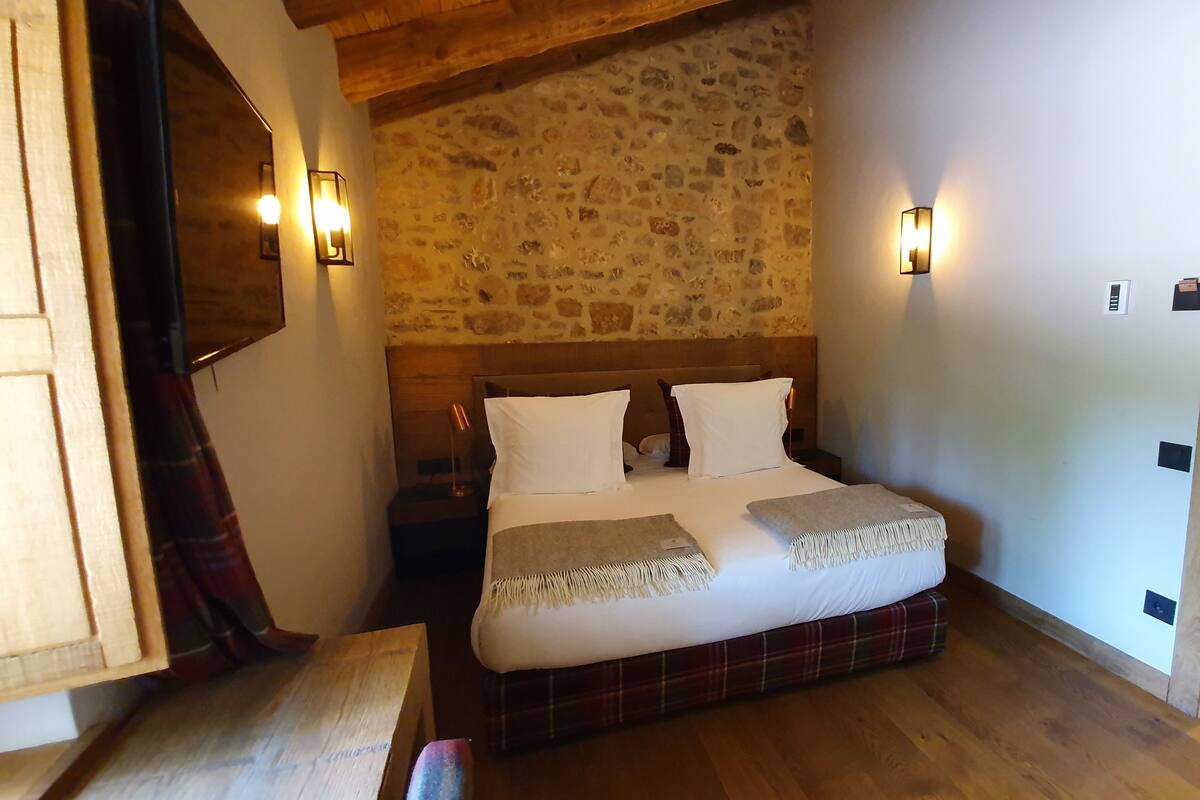 Ein Schlafzimmer mit einer Steinwand, Holzbalkendecke und einem Bett mit weißer Bettwäsche sowie zwei Nachttischen.