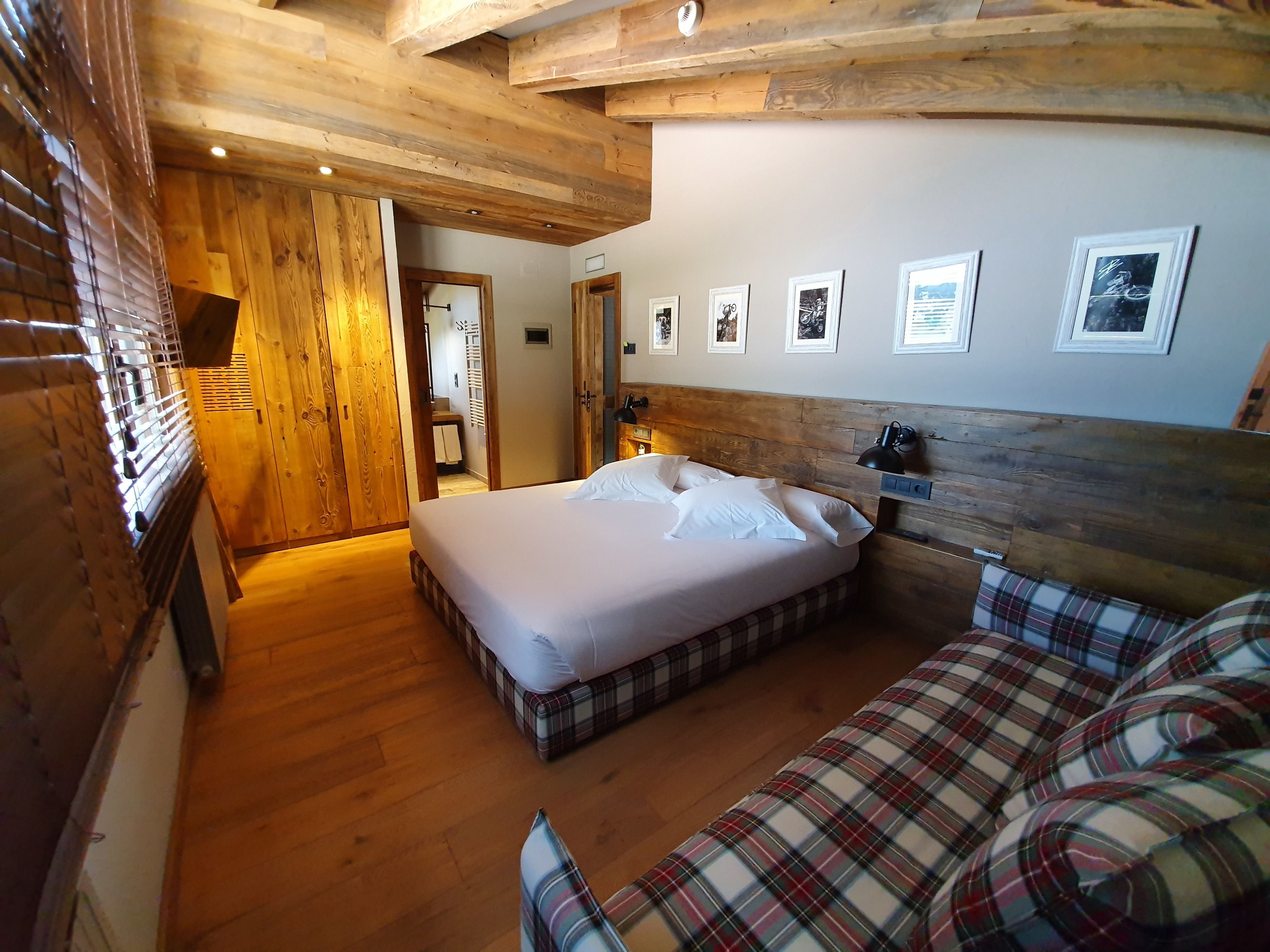 A cozy room with a bed, a sofa, wooden ceiling beams, and framed pictures on the wall.