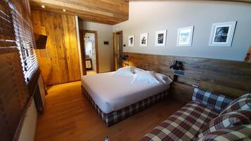 A cozy room with a bed, a sofa, wooden ceiling beams, and framed pictures on the wall.