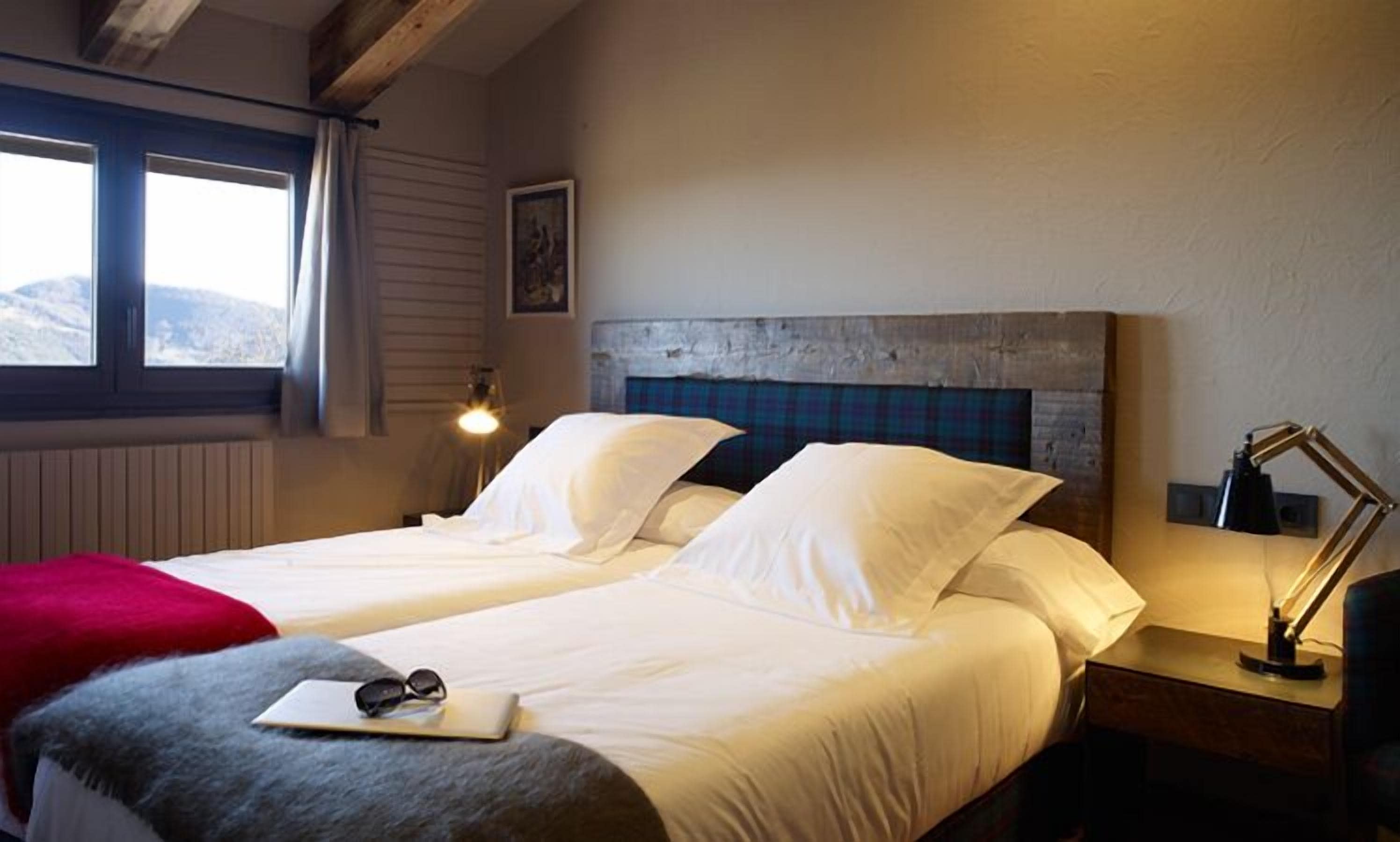 A double bed with white linens, a red throw blanket, and a pair of sunglasses on the bedside table.