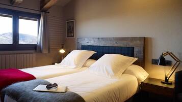 A double bed with white linens, a red throw blanket, and a pair of sunglasses on the bedside table.