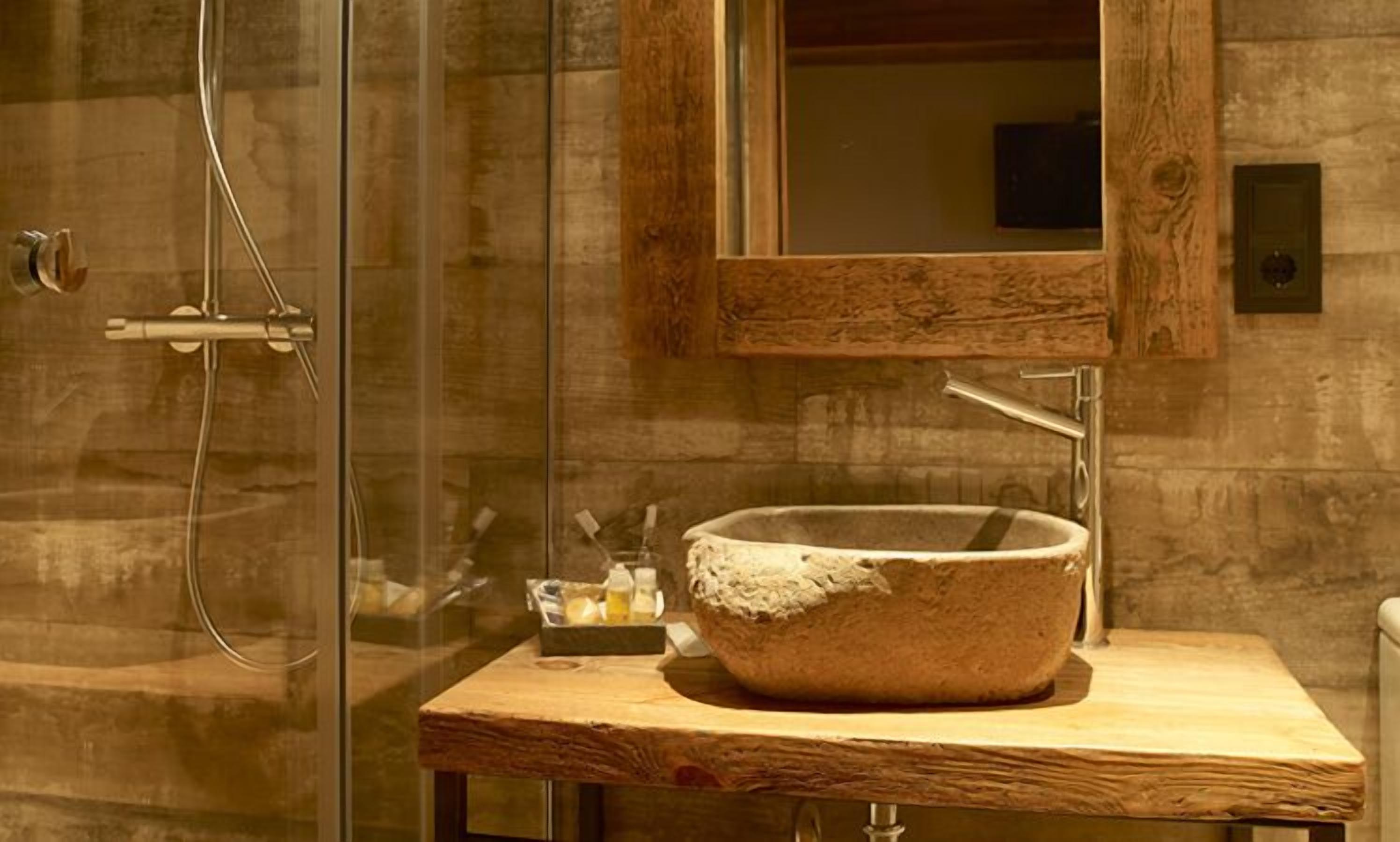 Un baño con lavamanos de piedra, tocador de madera y cabina de ducha de vidrio.