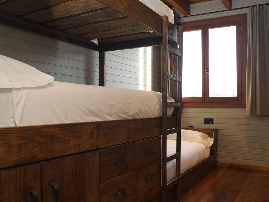 Ein Etagenbett mit Holz Kopfteil und Schubladen, ein Fenster mit Vorhängen und ein Holzboden.
